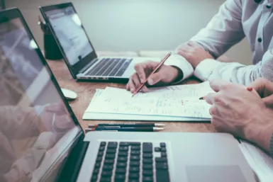 Ordinateur portable, personnes tenant un stylo devant une feuille de calcul